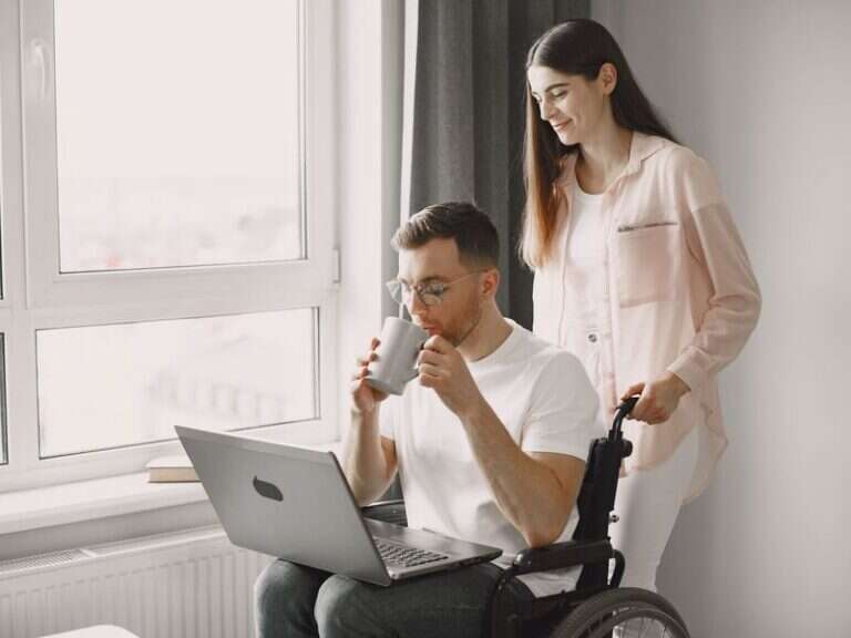 A support worker and a man using a wheelchair sharing coffee at home