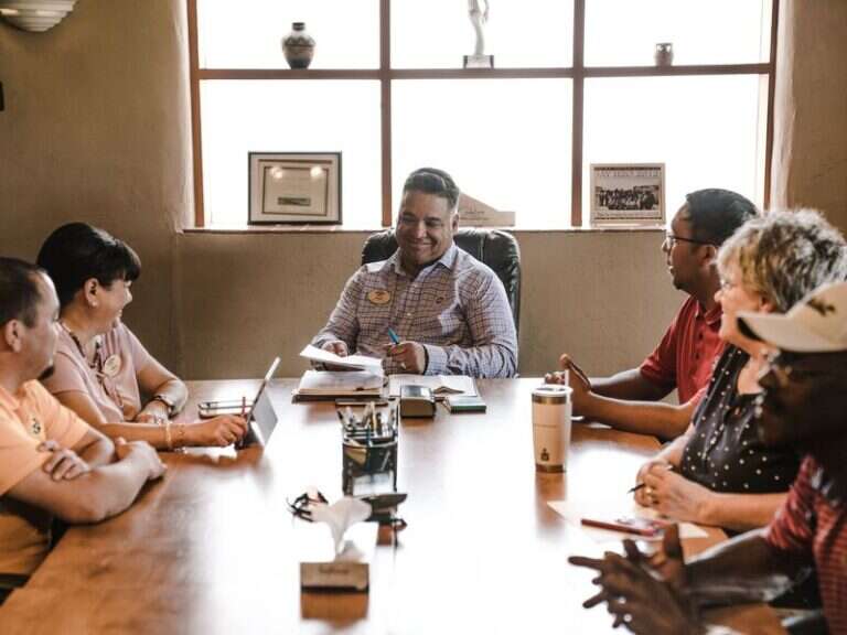 A mixed group of adults in discussion around a long wooden table