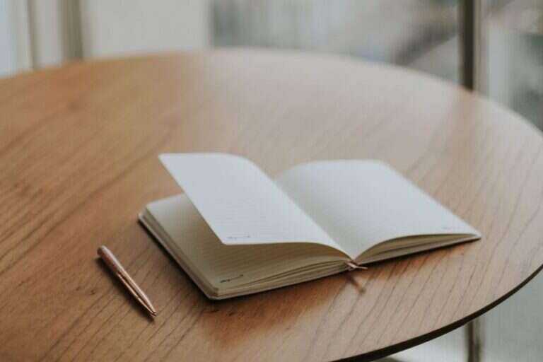 An open journal on a wooden table beside a window