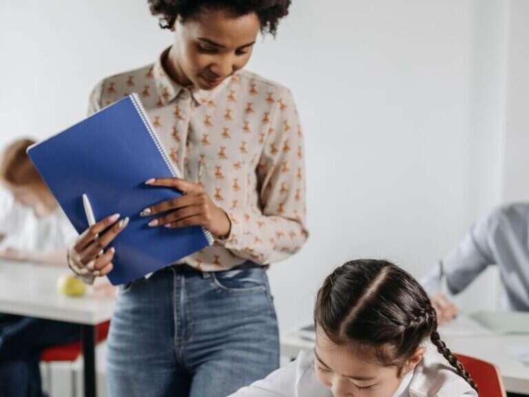 A teacher looking over a student’s work in a bright classroom
