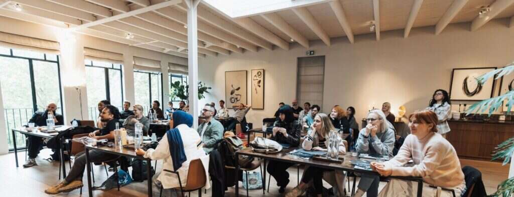 A bright, skylit room with participants seated at long tables during a workshop session